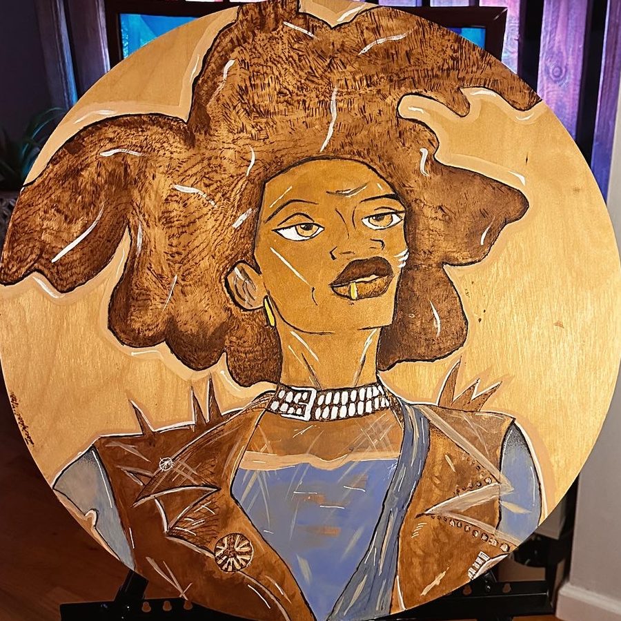 I don&rsquo;t believe in consistency, a round wood burning and acrylic painting of a woman with voluminous burned-wood hair, a pearl choker, a studded leather vest and a blue top.
